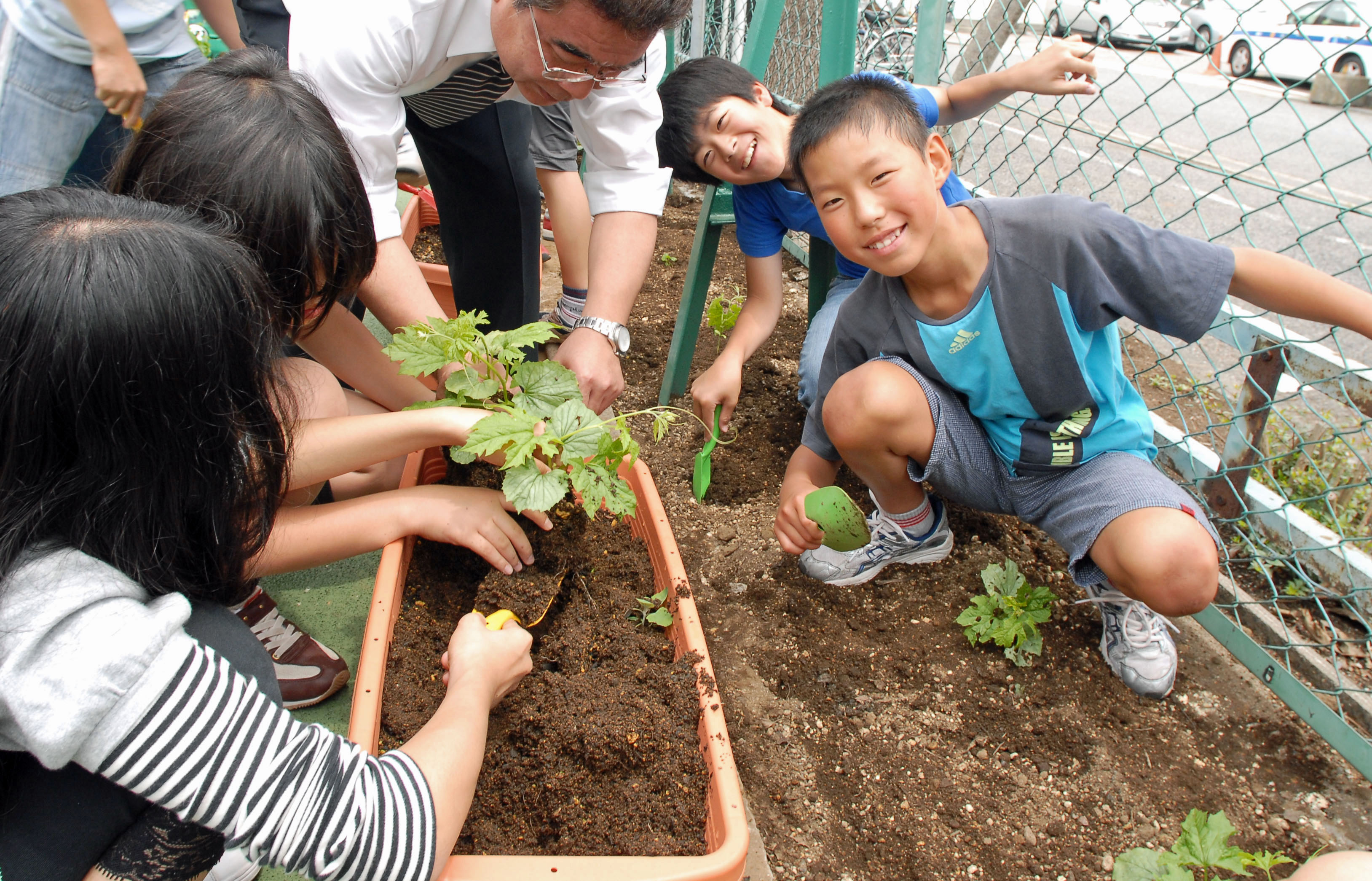 Several community members helping to teach several cheerful children about garden plots.